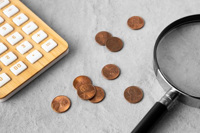 Moedas numa mesa onde se vê ainda uma lupa e uma calculadora.